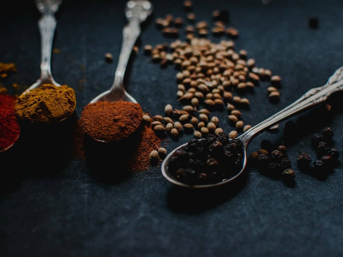 Ground spices and peppercorns on antique spoons against dark slate
