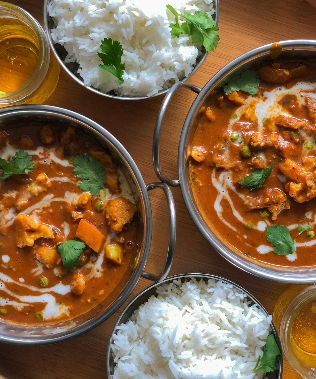 Bowls of Indian curry and steamed rice on a wooden table