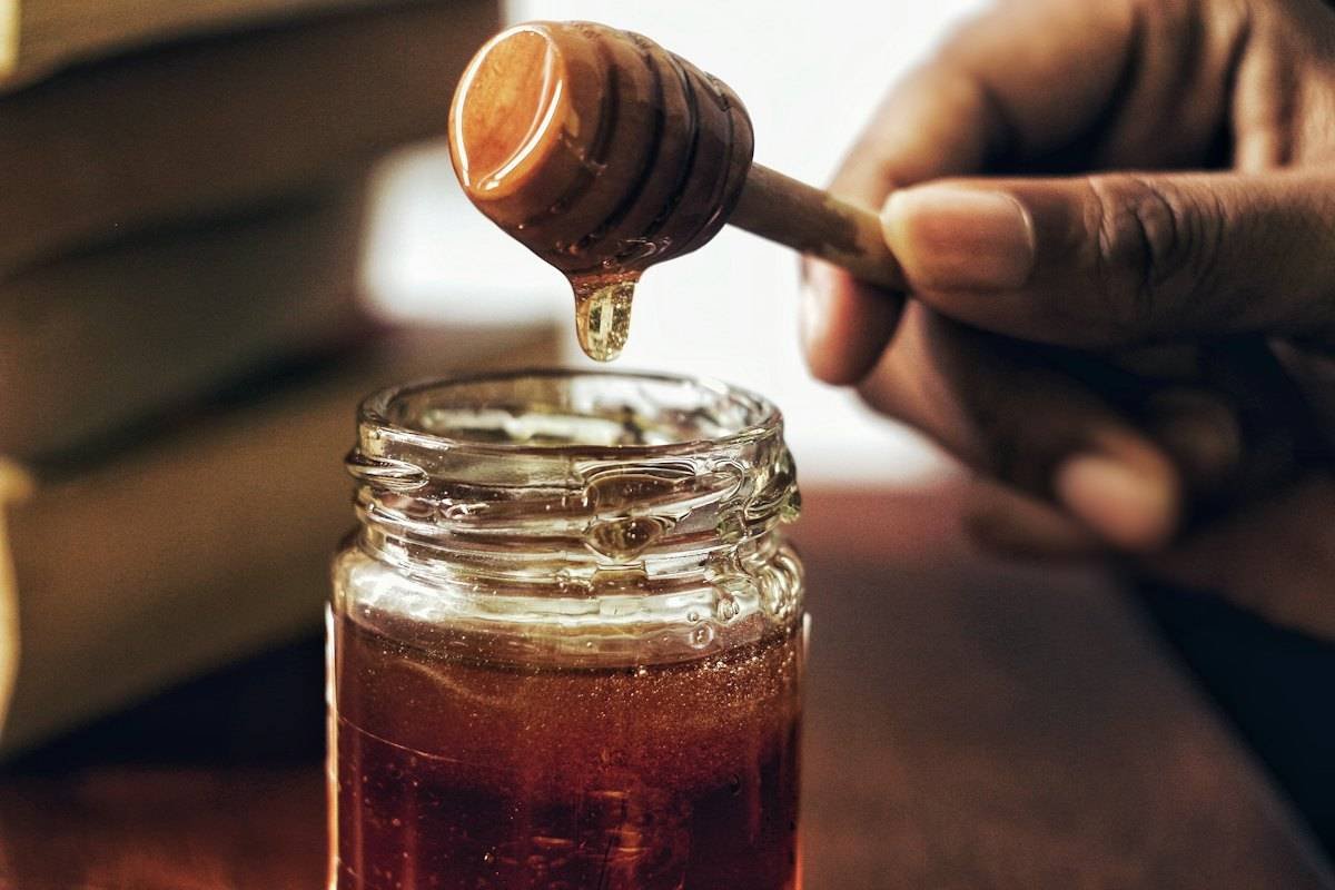 Amber syrup dripping from a wooden dipper into a glass jar